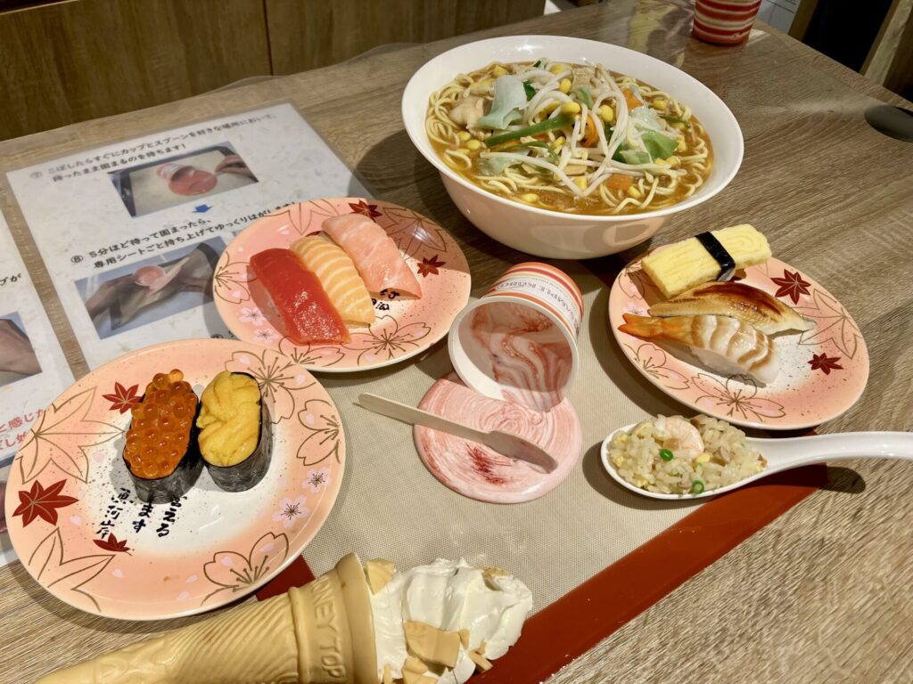 机の上にカップアイス、ラーメン、寿司の食品サンプルが置かれている